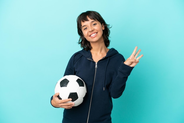 Young mixed race football player woman isolated on blue background happy and counting three with fingers