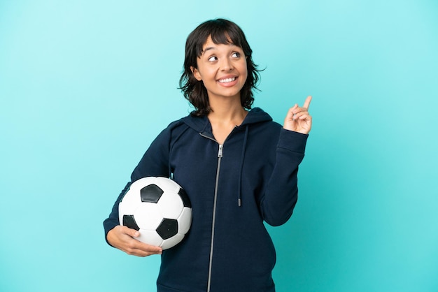 Young mixed race football player woman isolated on blue background pointing up a great idea