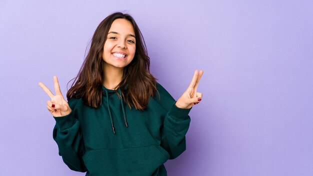 Young mixed race hispanic woman isolated showing victory sign and smiling broadly.