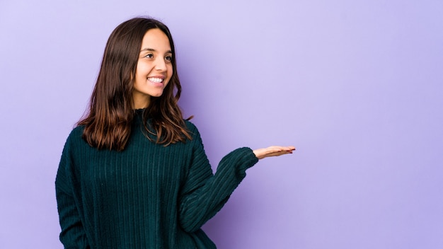 Young mixed race hispanic woman showing a copy space on a palm and holding another hand on waist.