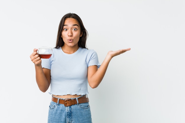 Young mixed race indian holding a tea cup impressed holding copy space on palm.