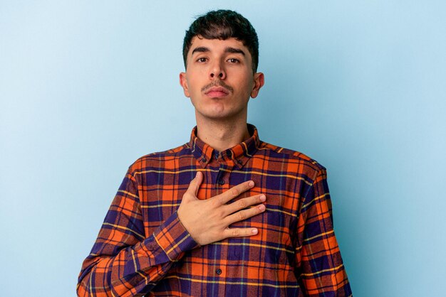 Young mixed race man isolated on blue background taking an oath, putting hand on chest.