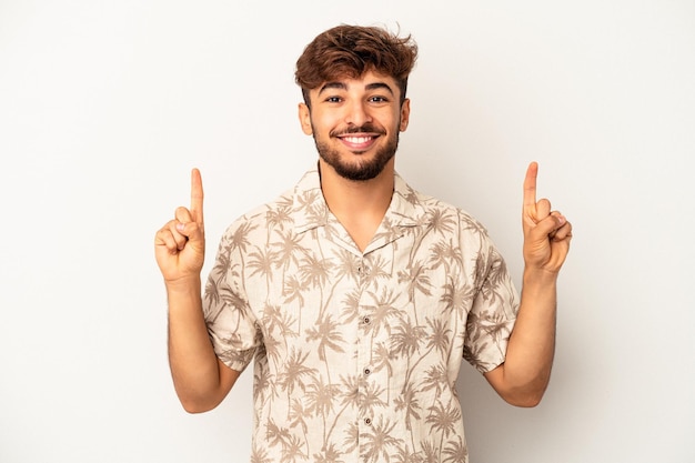 Young mixed race man isolated on grey background indicates with both fore fingers up showing a blank space.