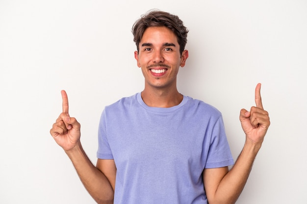 Young mixed race man isolated on white background indicates with both fore fingers up showing a blank space.