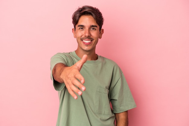 Young mixed race man isolated on white background stretching hand at camera in greeting gesture.