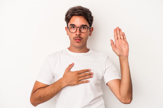 Young mixed race man isolated on white background taking an oath, putting hand on chest.