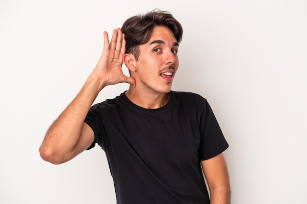 Young mixed race man isolated on white background trying to listening a gossip.