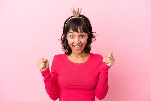 Young mixed race princess with crown isolated on pink background celebrating a victory in winner position