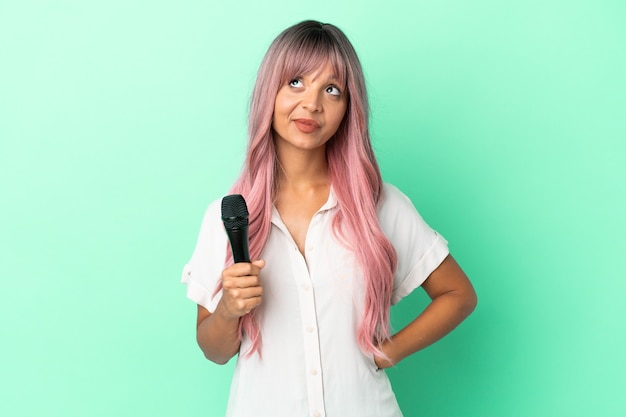 Young mixed race singer woman with pink hair isolated on green background and looking up