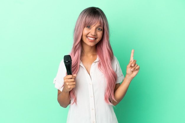 Young mixed race singer woman with pink hair isolated on green background pointing up a great idea