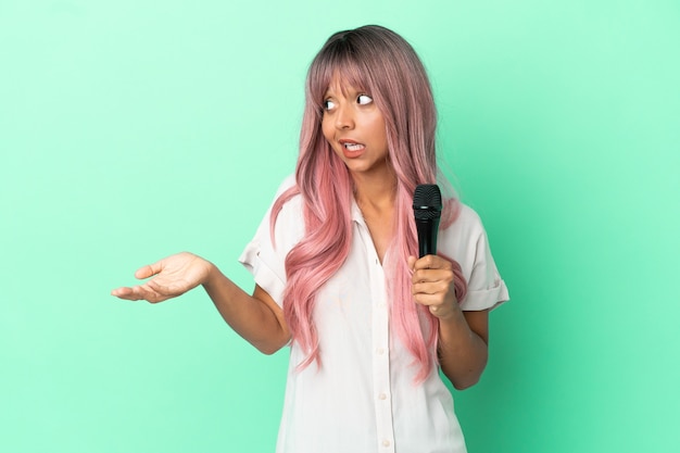 Young mixed race singer woman with pink hair isolated on green background with surprise expression while looking side