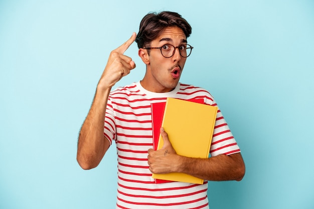 Young mixed race student man holding books isolated on blue background having an idea, inspiration concept.