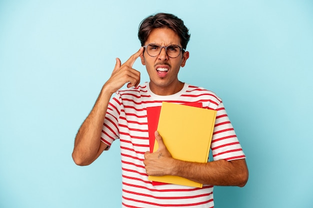 Young mixed race student man holding books isolated on blue background showing a disappointment gesture with forefinger.