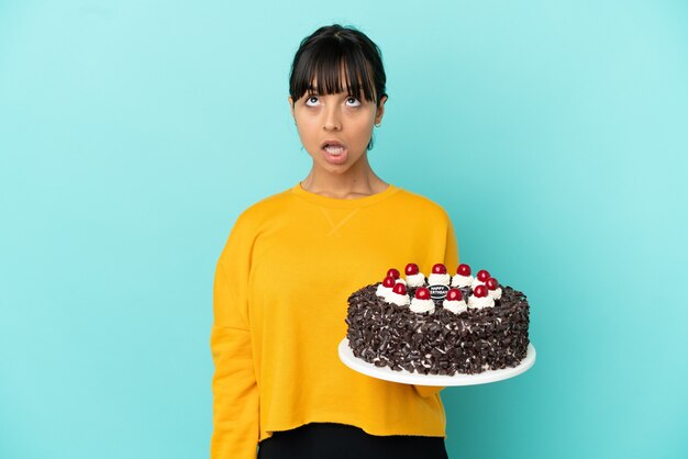 Young mixed race woman holding birthday cake looking up and with surprised expression