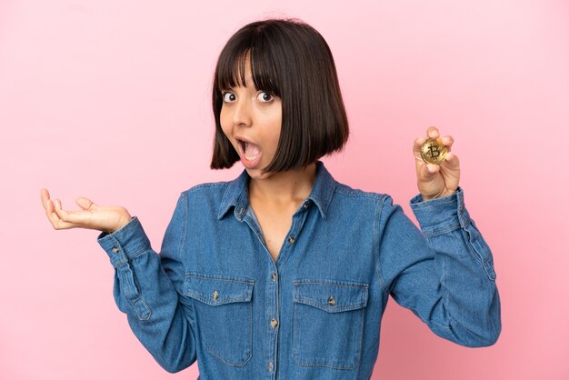 Photo young mixed race woman holding a bitcoin isolated background with shocked facial expression