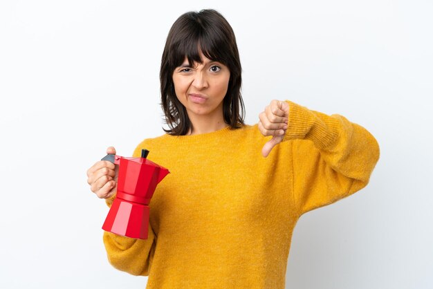 Young mixed race woman holding coffee pot isolated on white background showing thumb down with negative expression