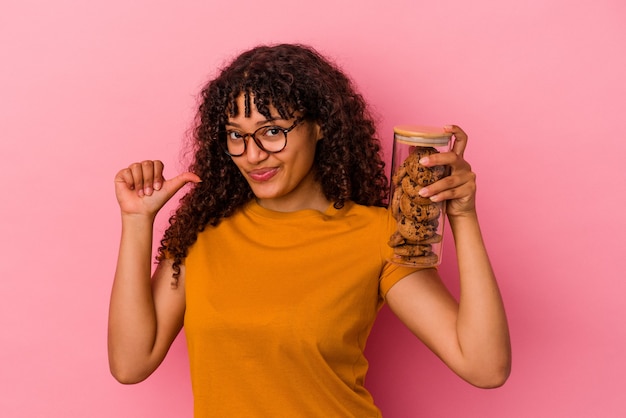 Young mixed race woman holding a cookies jar isolated on pink background feels proud and self confident, example to follow.