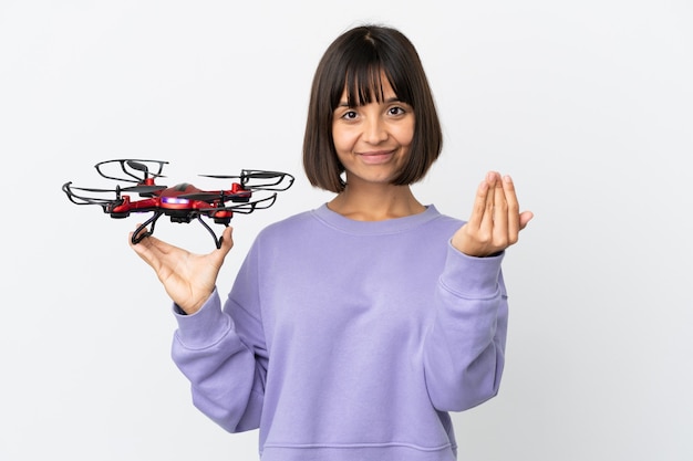 Young mixed race woman holding a drone isolated on white background inviting to come with hand. Happy that you came