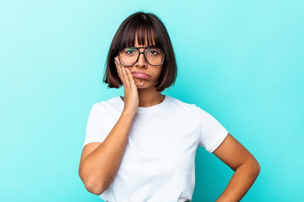 Young mixed race woman isolated on blue background blows cheeks, has tired expression. Facial expression concept.