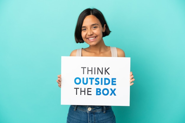 Young mixed race woman isolated on blue background holding a placard with text Think Outside The Box