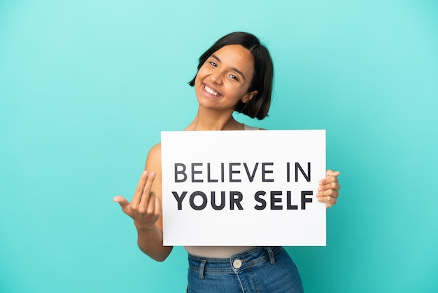 Young mixed race woman isolated on blue background holding We Want You board and doing coming gesture