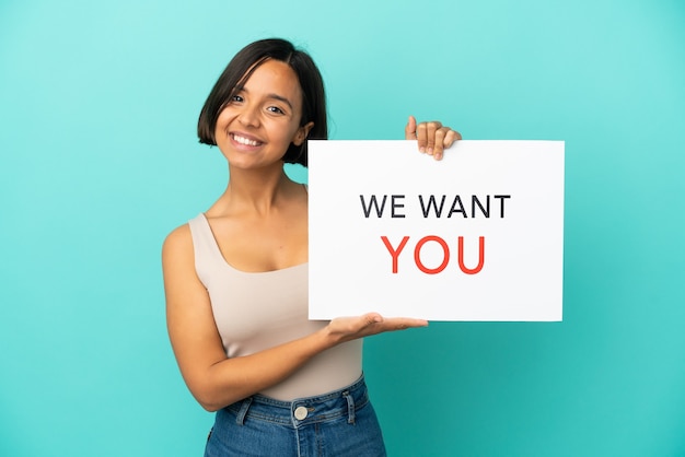 Young mixed race woman isolated on blue background holding We Want You board with happy expression