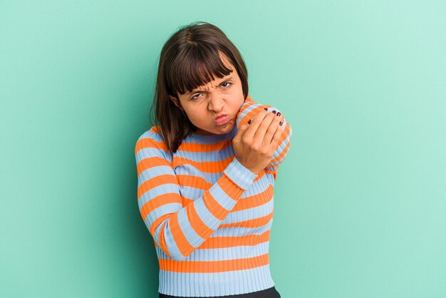 Young mixed race woman isolated on blue background massaging elbow, suffering after a bad movement.