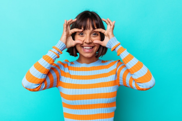 Young mixed race woman isolated on blue background showing okay sign over eyes