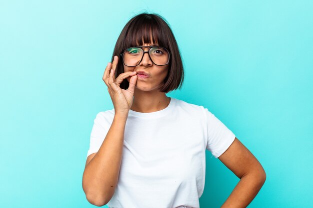 Young mixed race woman isolated on blue background with fingers on lips keeping a secret.