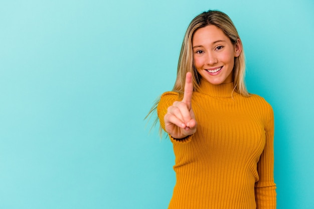 Young mixed race woman isolated on blue showing number one with finger.