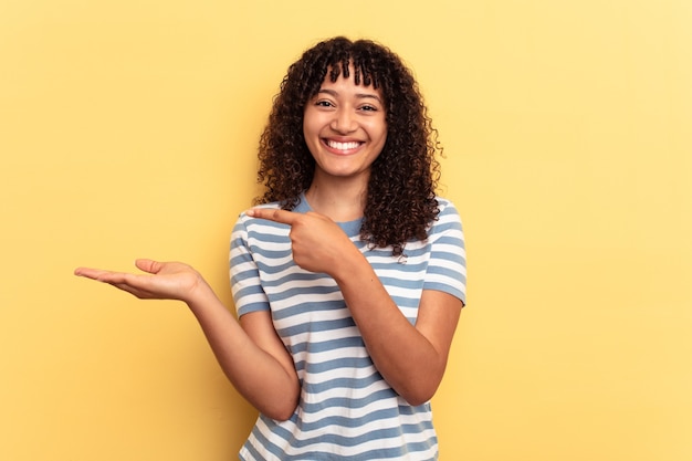 Young mixed race woman isolated on yellow background excited holding a copy space on palm.