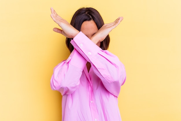 Young mixed race woman isolated on yellow background keeping two arms crossed, denial concept.