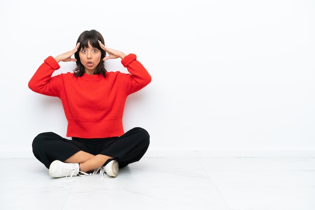 Young mixed race woman sitting on the floor isolated on white background with surprise expression