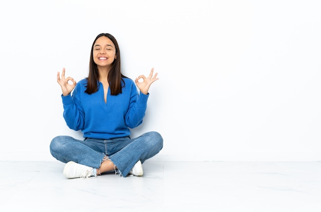 Young mixed race woman sitting on the floor isolated on white background in zen pose