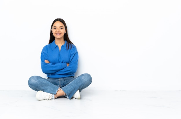 Young mixed race woman sitting on the floor isolated on white keeping the arms crossed in frontal position