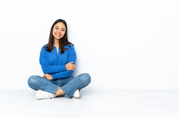 Young mixed race woman sitting on the floor isolated on white laughing