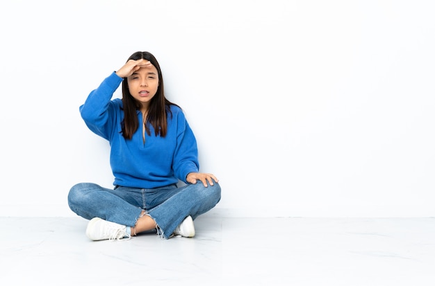 Young mixed race woman sitting on the floor isolated on white looking far away with hand to look something