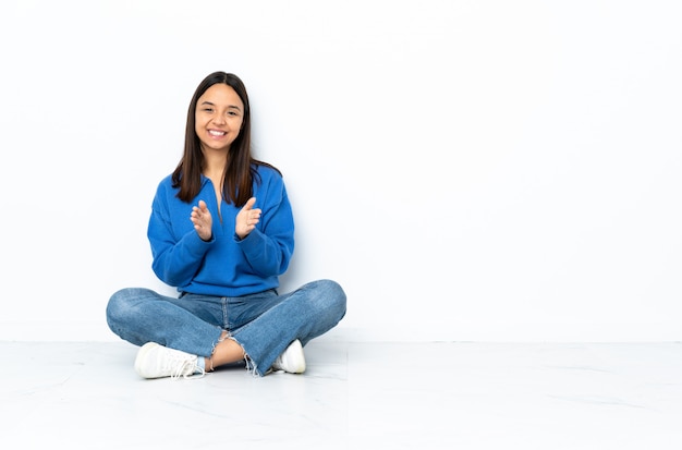 Young mixed race woman sitting on the floor isolated on white wall applauding after presentation in a conference