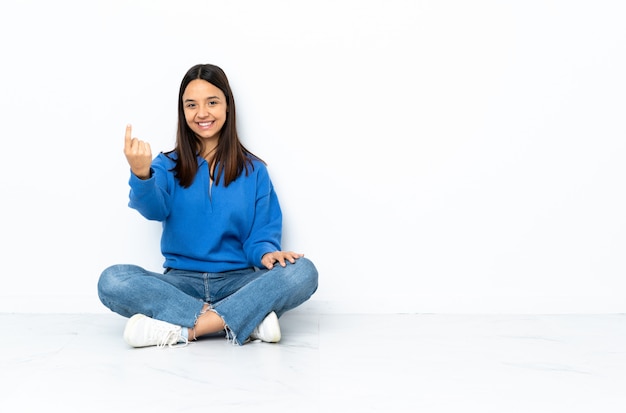 Young mixed race woman sitting on the floor isolated on white wall doing coming gesture