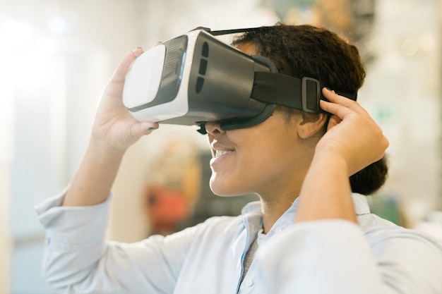 Young mixed-race woman taking on vr headset on head to watch presentation of new assortment and choose product