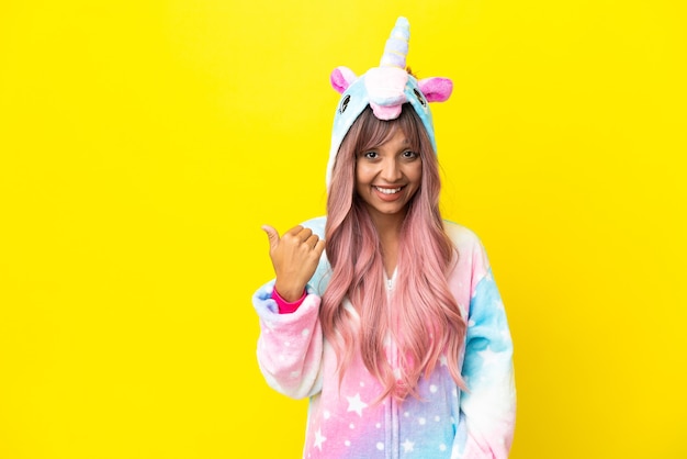 Young mixed race woman wearing a unicorn pajama isolated on white background pointing to the side to present a product