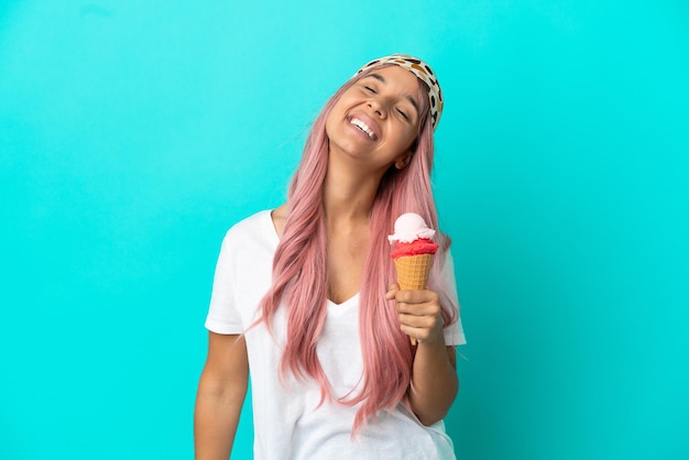 Young mixed race woman with a cornet ice cream isolated on blue background laughing