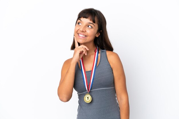 Young mixed race woman with medals isolated on white background thinking an idea while looking up