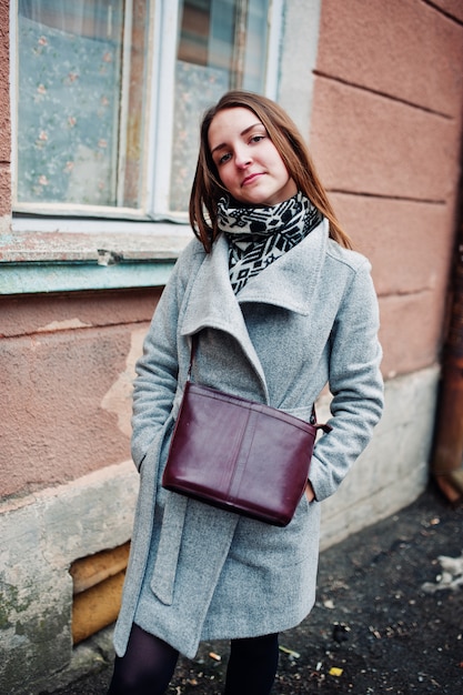 Young model girl in a gray coat with leather handbag on shoulders 