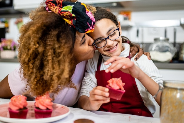 Young mom hugging and kissing her daughter while cooking cakes together for a party