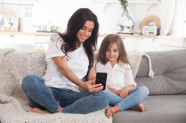 Young mom and little daughter playing online games at home using a smartphone