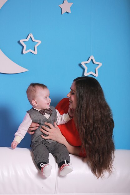 Young mom with cute baby boy on a white sofa. blue wall with a white moon and stars on a wall.