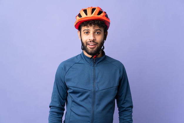 Young Moroccan cyclist man isolated on purple with surprise facial expression