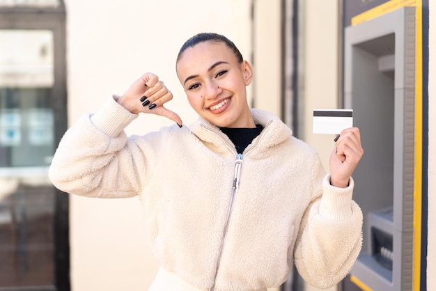 Young moroccan girl holding a credit card at outdoors proud and selfsatisfied