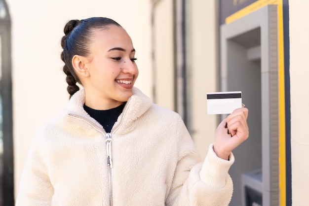 Young moroccan girl holding a credit card at outdoors with happy expression